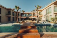 A wooden walkway crossing the pool in the palm-lined courtyard at INZA Ovacık, with terracotta umbrellas beyond