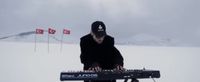 A musician playing a keyboard on a snowfield with Turkish flags behind